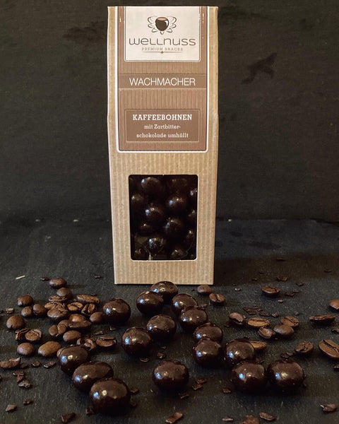 Wachmacher Kaffeebohnen mit Zartbitterschokolade in stilvoller Verpackung, umgeben von Kaffeebohnen. Genussvolle Energiequelle für zwischendurch.