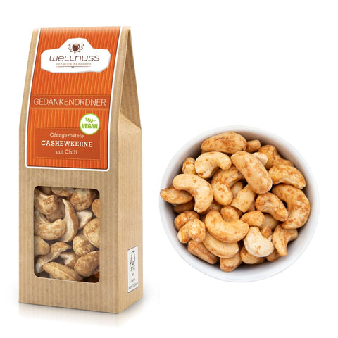 Gedankenordner - Ofengeröstete Cashewkerne mit Chili (60 g) in nachhaltiger Verpackung mit Sichtfenster, daneben eine Schale mit gewürzten Cashews.