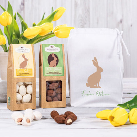 Baumwollsäckchen mit Osterdesign und zwei Ostersnacks, bestehend aus weißen Schoko-Mandeln und Trüffelmandeln. Nachhaltige Geschenkverpackung für Ostern.