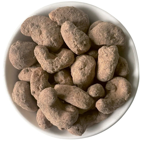Nahaufnahme karamellisierter Cashewkerne mit Orange & Kakao in einer weißen Schale. Die knackigen Nüsse sind mit feinem Kakaopulver umhüllt.